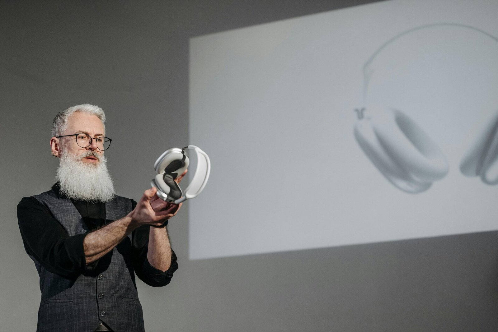 A bearded man presenting a pair of wireless headphones during a business meeting.